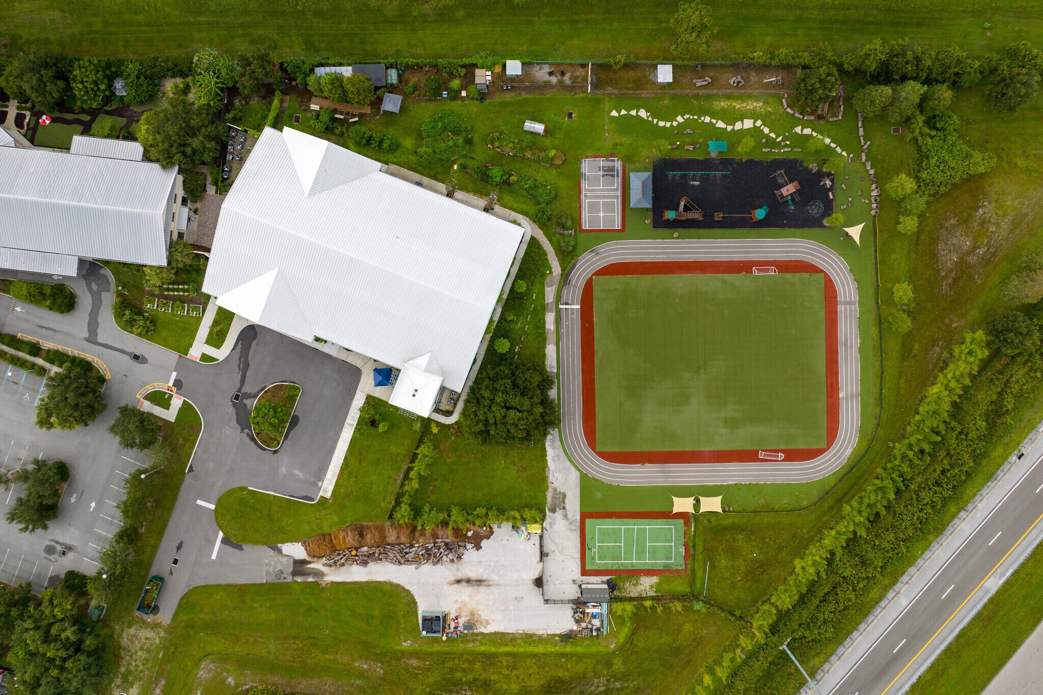 Aerial of the Creation Village World School campus — buildings, track, courts, drop-off loop, and parking read as one operation