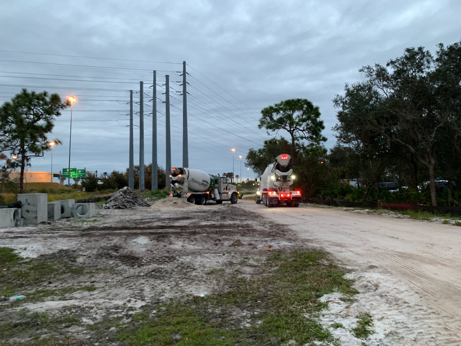 Concrete mixer trucks staged at the Creation Village school site at dusk