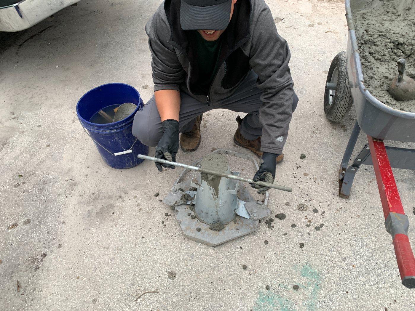 A crew member performing a concrete slump test beside a wheelbarrow of fresh mix