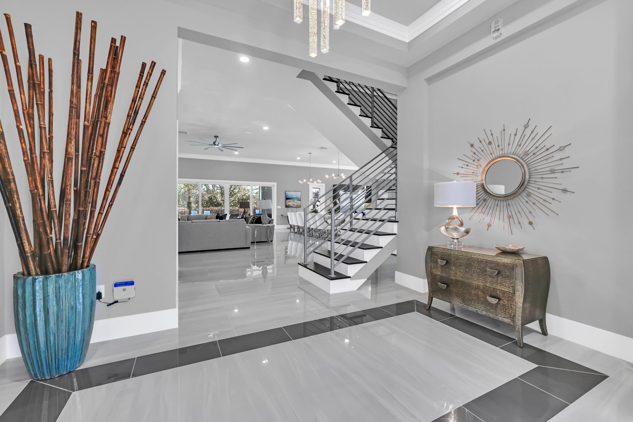 Grand entry foyer with a floating staircase, sunburst mirror, and a tall bamboo vessel