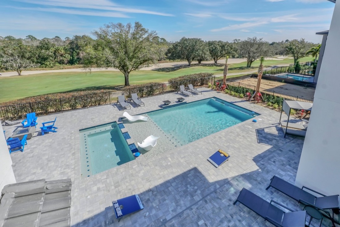 Covered lanai lounge under a wood ceiling, open to the lit pool at dusk with the summer kitchen alongside