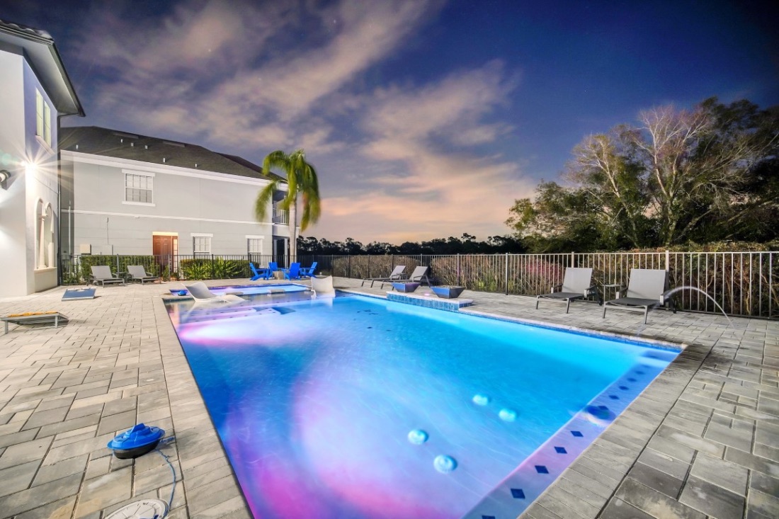 Resort pool glowing at twilight, with loungers, palms, and a dusk sky