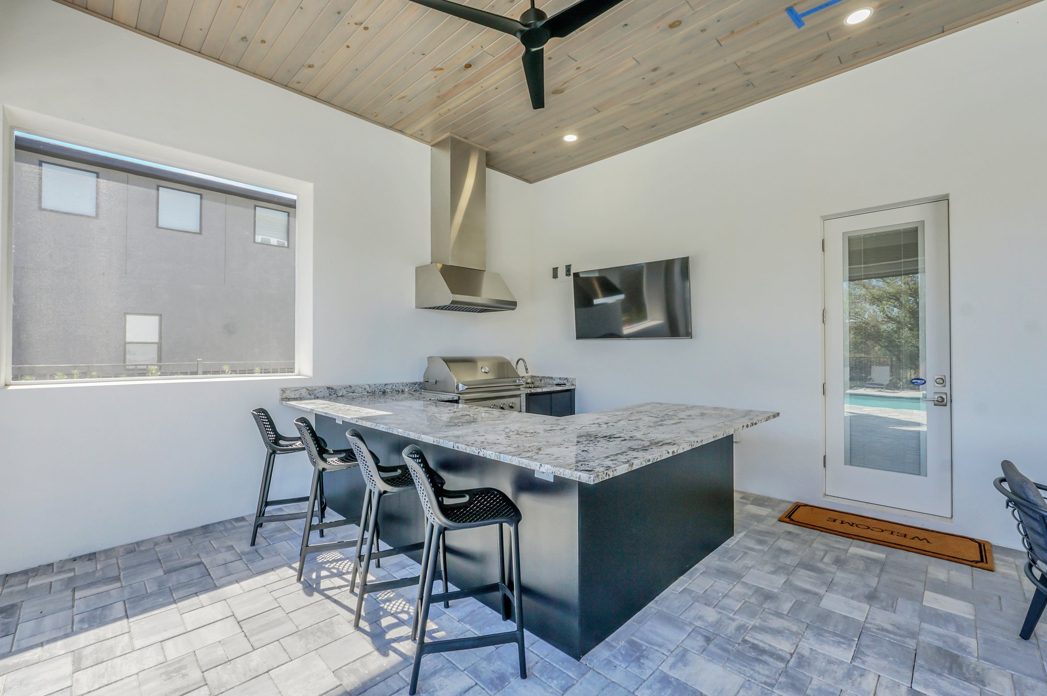 Covered summer kitchen with a built-in grill, bar seating, and a TV under the lanai