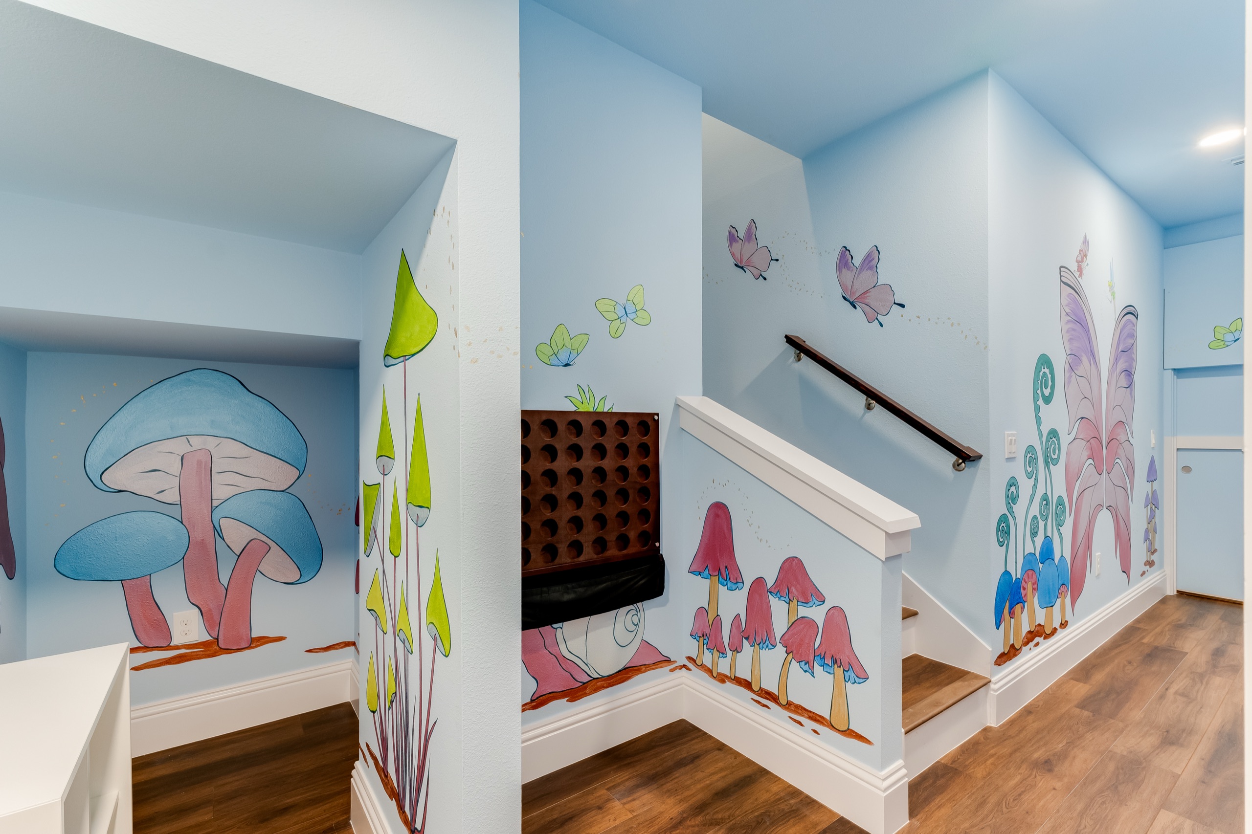 Loft playroom stair with a hand-painted mushroom-and-butterfly fairy-garden mural and a wall Connect Four