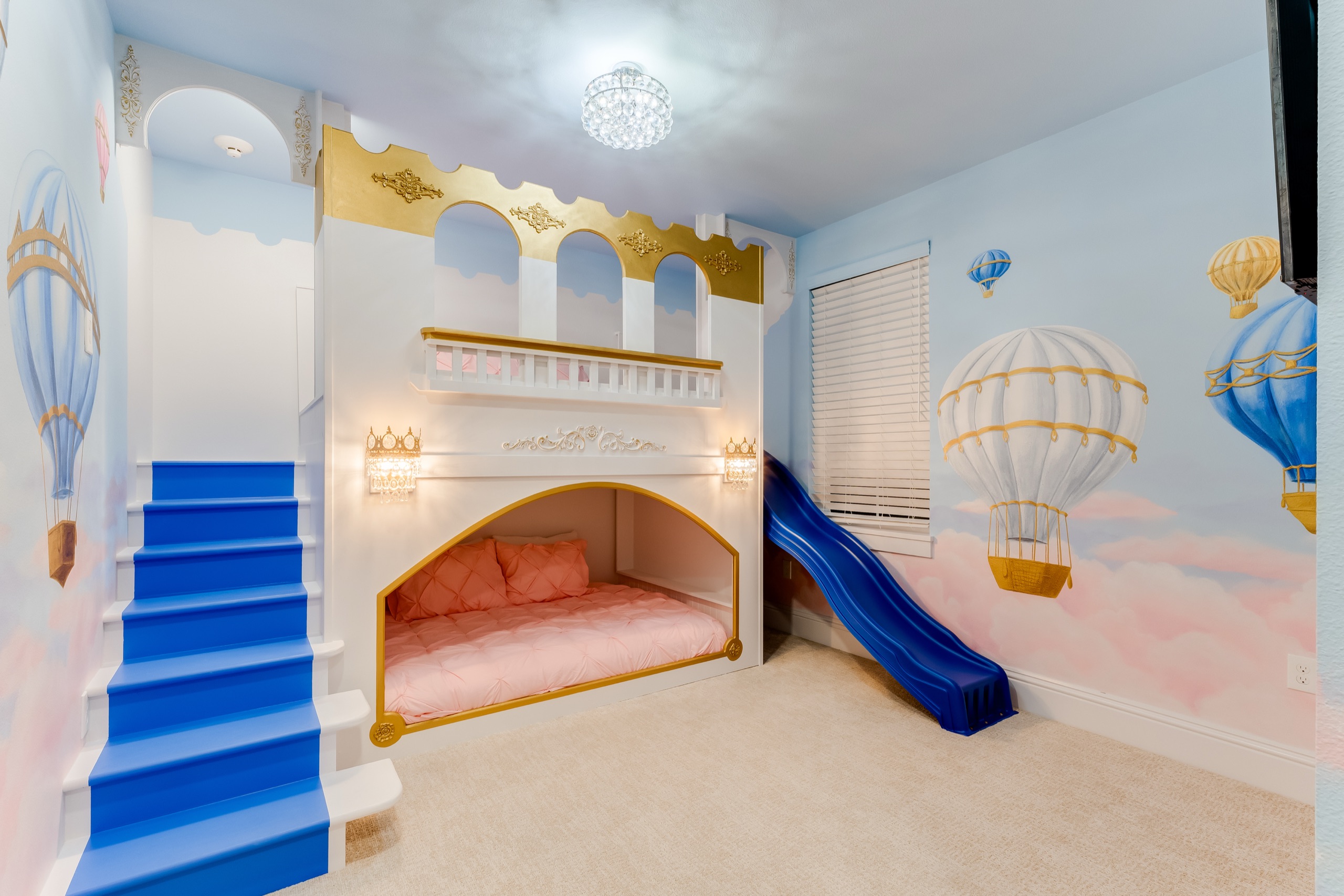 Princess bedroom with a white castle bunk, blue slide, and a hot-air-balloon mural