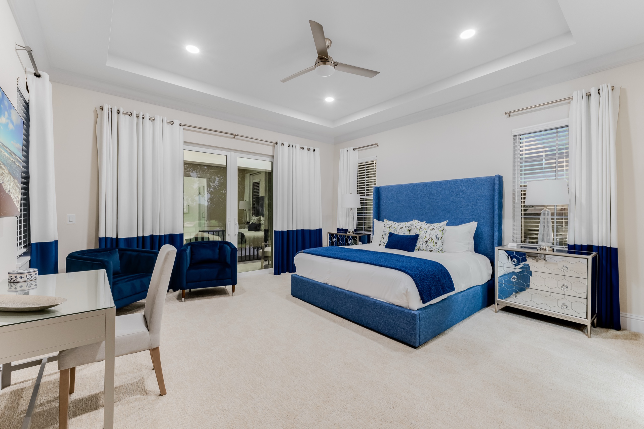 An upstairs en-suite bedroom with a blue velvet bed, sitting chairs, and a writing desk