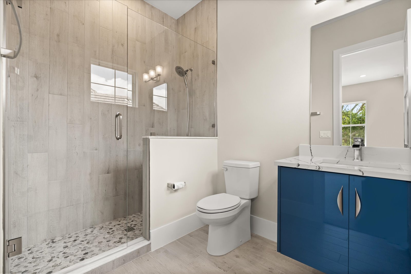 Wood-look tiled walk-in shower beside a blue vanity
