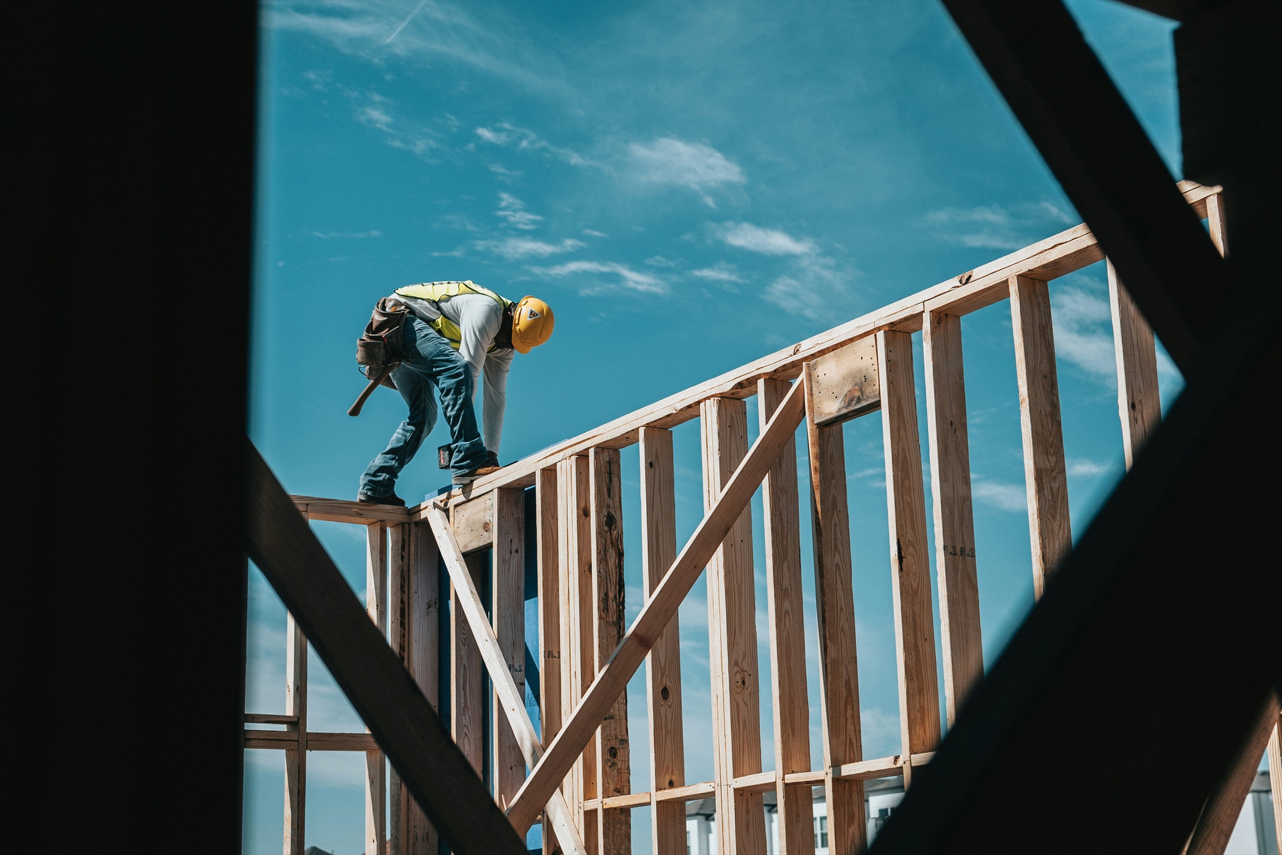 A framer working atop wall framing against a blue sky on a Liberty build