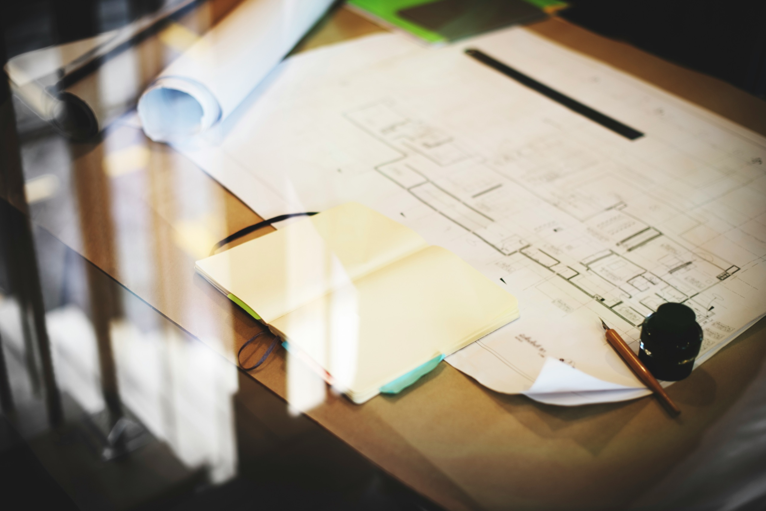 An open sketchbook, drafting pen, and floor plans on a sunlit studio desk