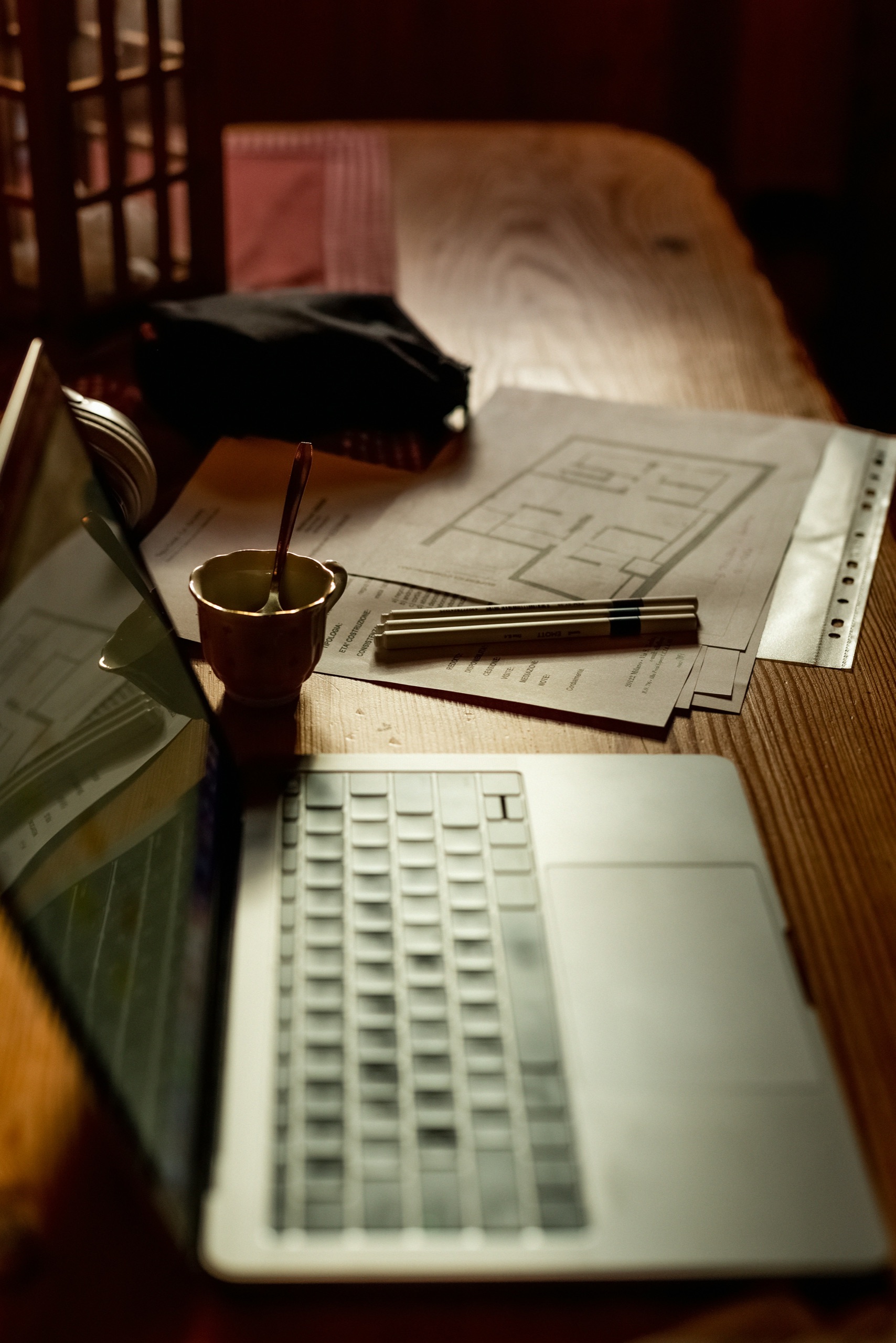 A laptop, floor plans, and specification documents on a warmly lit desk
