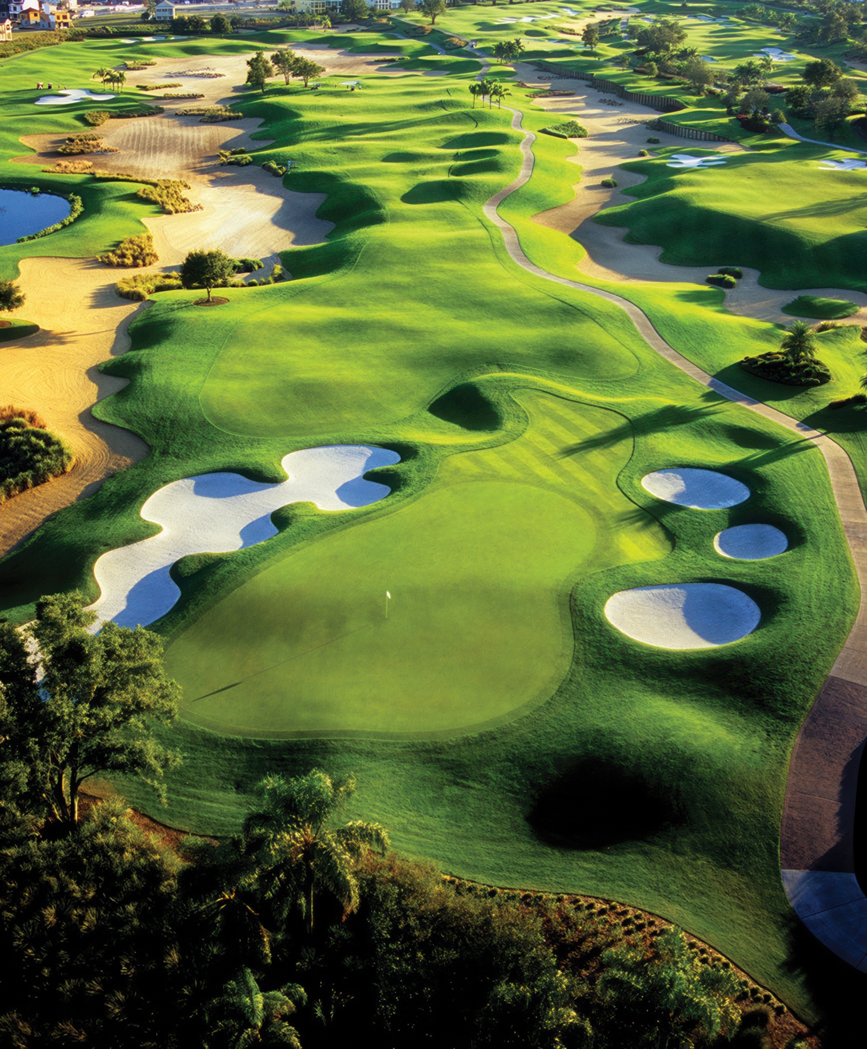 Aerial view down a Reunion signature fairway — bunkers, water, and cart path at golden hour