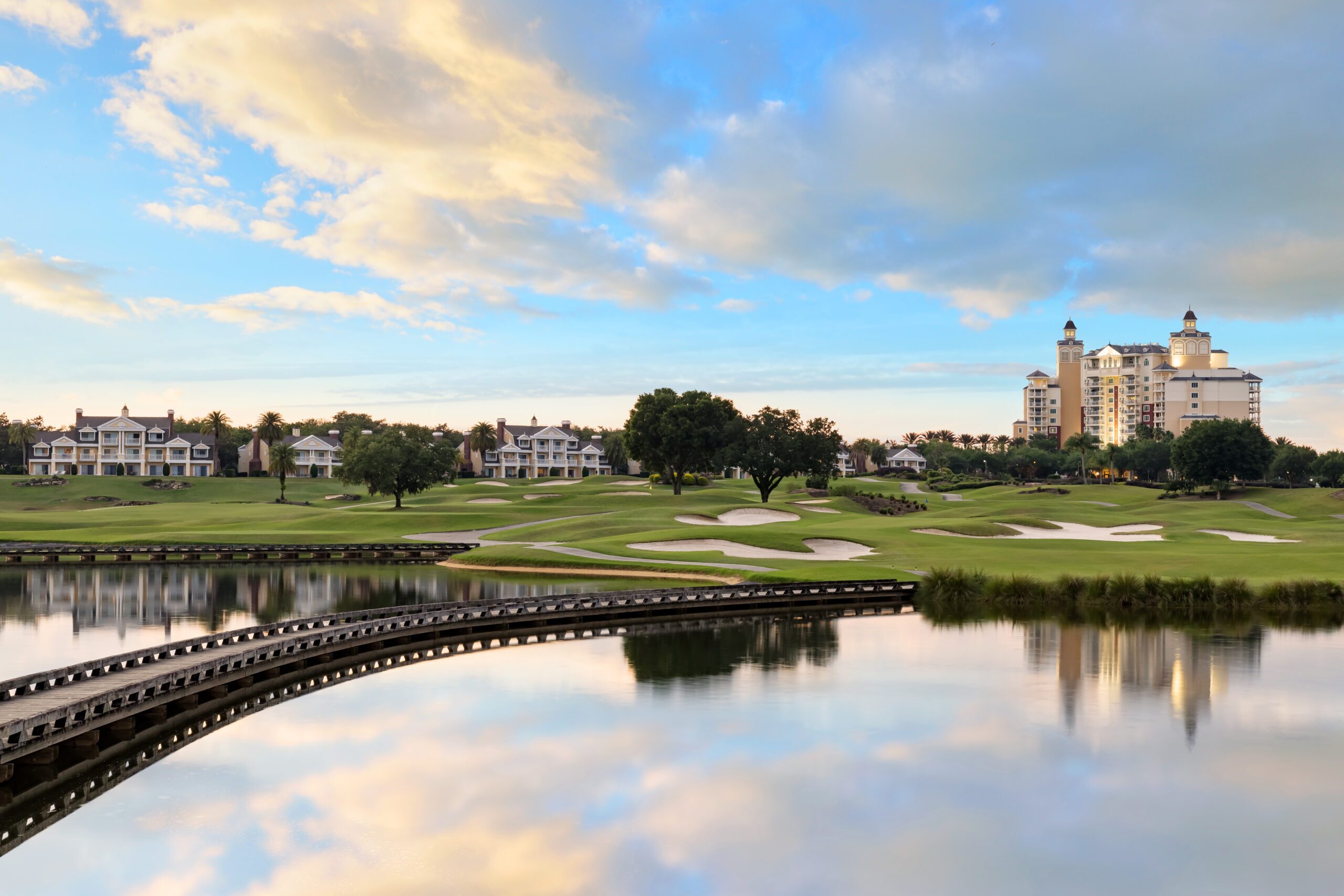Reunion Resort at dusk — villas and the grande clubhouse reflected across the water beyond the boardwalk