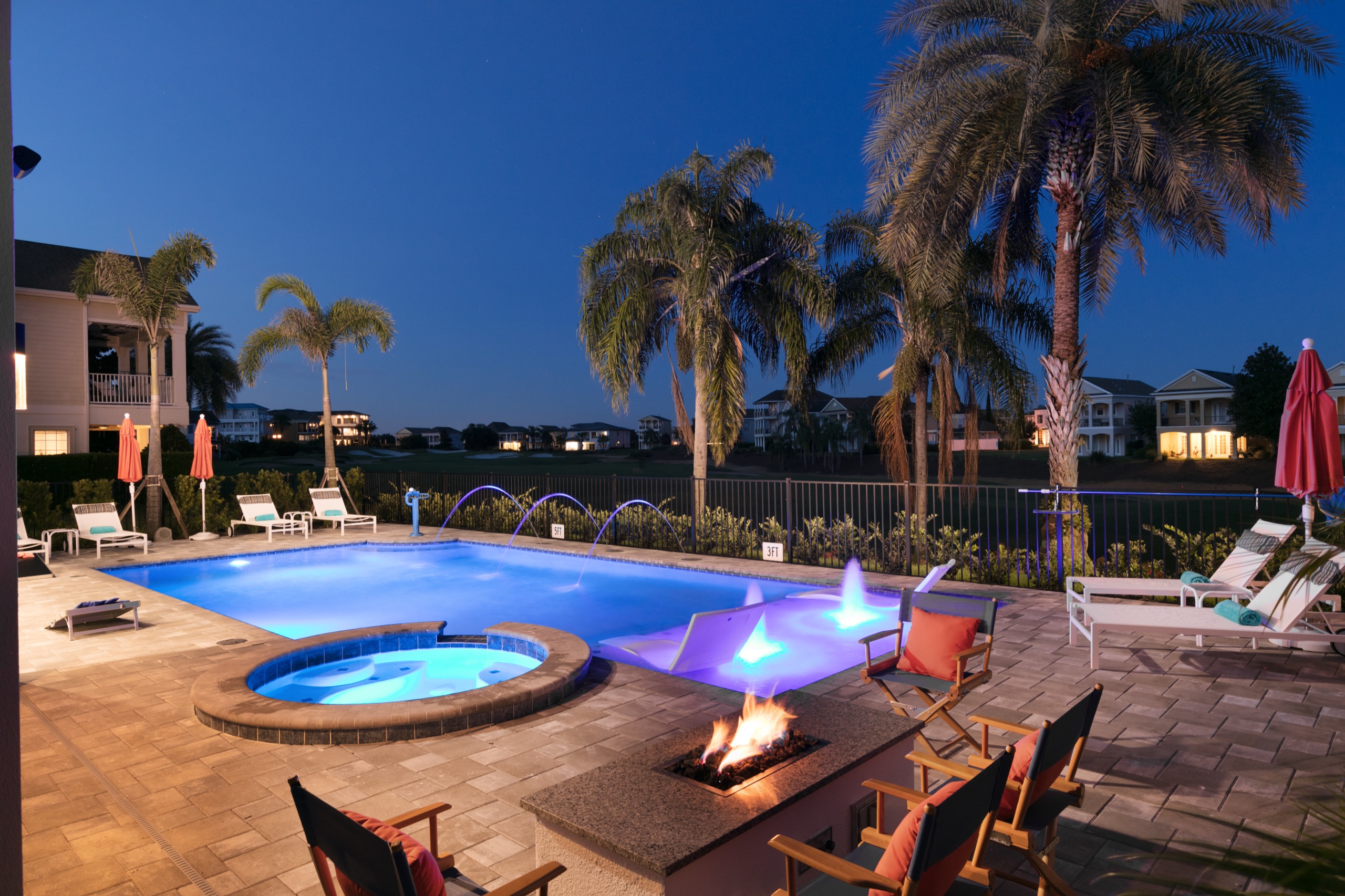 Radiant Street — lit pool with deck jets, spa, and a fire pit at dusk, the championship fairway just beyond the fence
