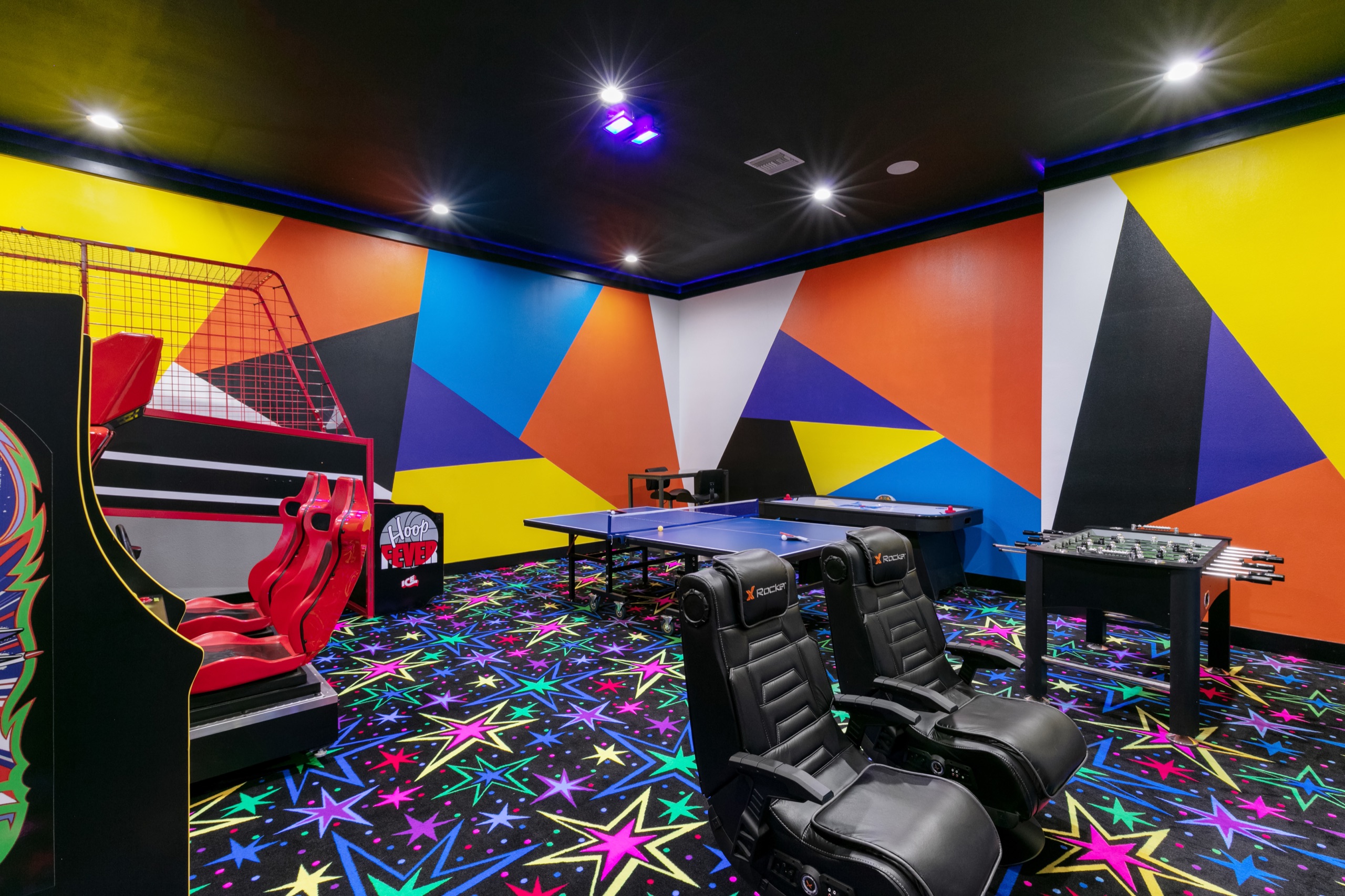 Game room with ping-pong, foosball, and racing rigs under neon walls