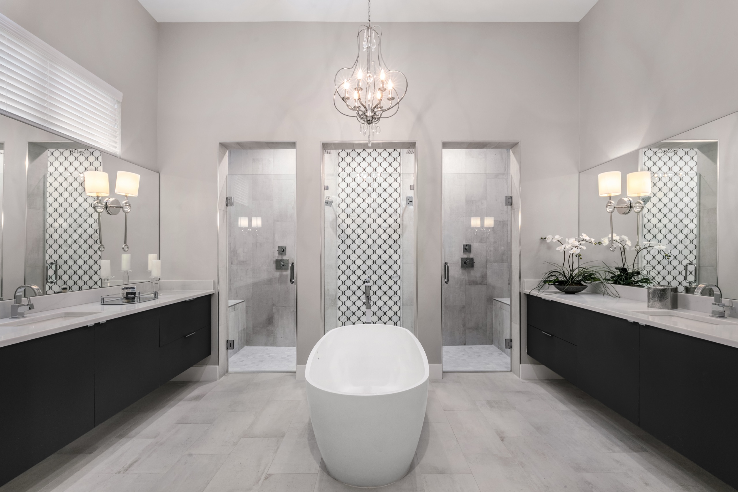 Primary bath with twin floating vanities, a freestanding tub, dual walk-in showers, and a crystal chandelier