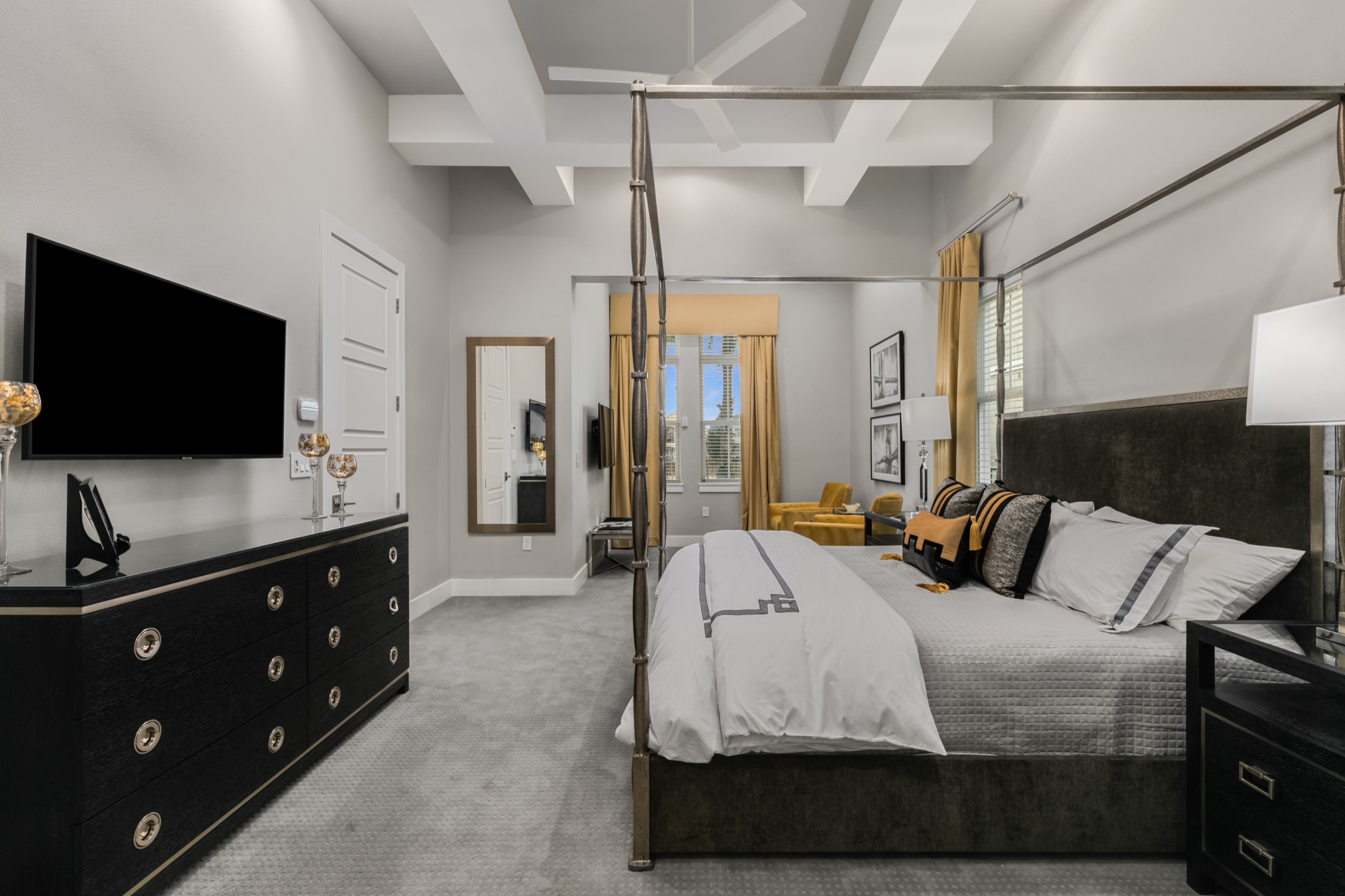 Primary suite with a wrought-iron canopy bed, coffered ceiling, gold accents, and a private sitting area