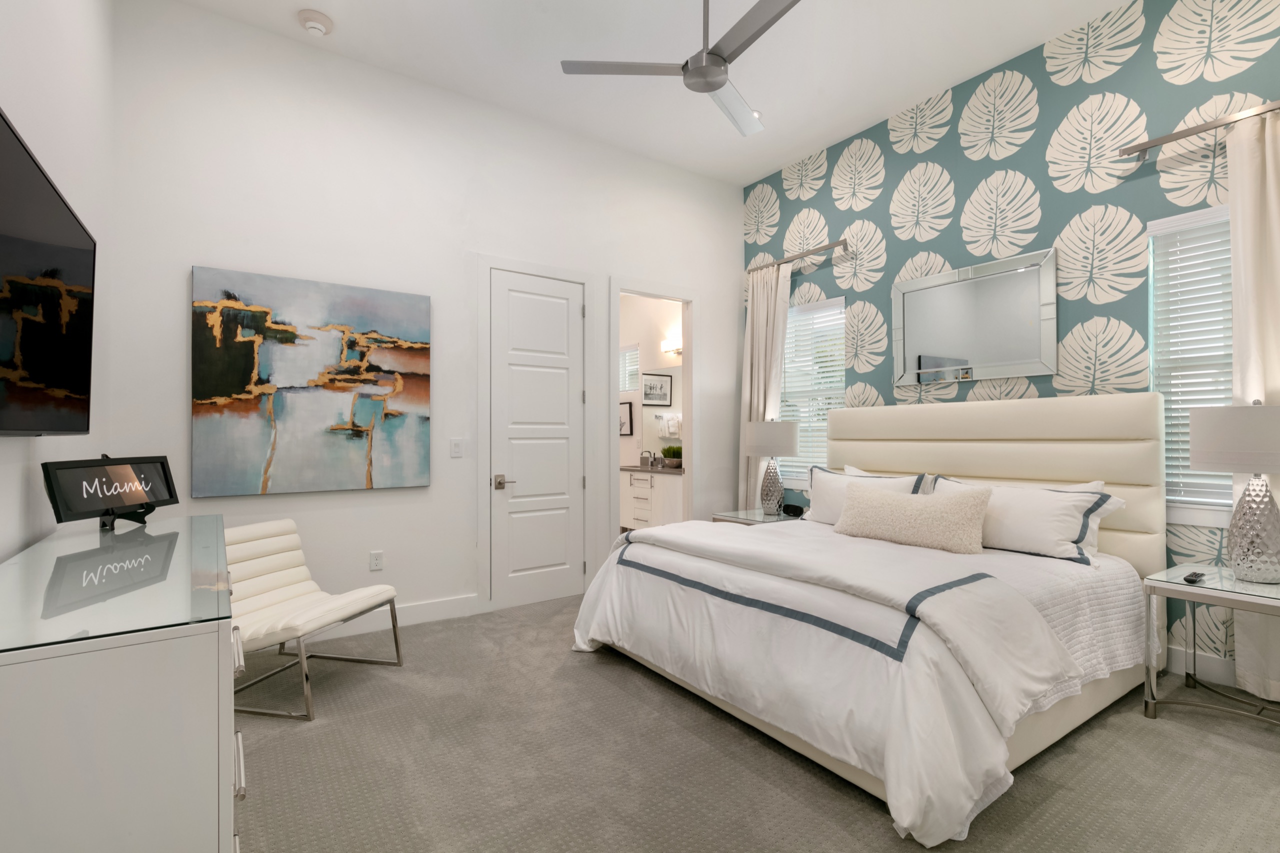 Miami suite with a monstera-leaf accent wall, white leather headboard, and an en-suite beyond