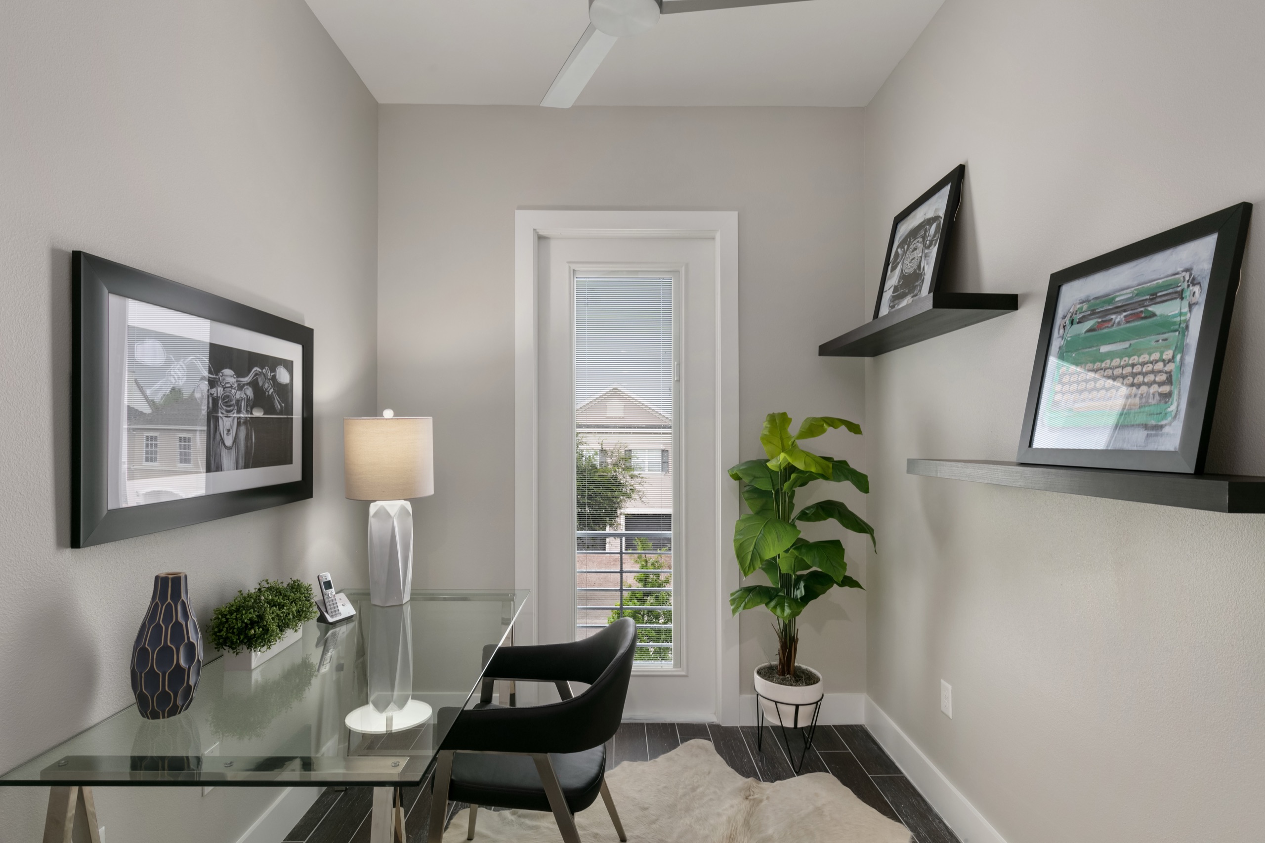 Home office with a glass desk, black leather chair, and framed vintage typewriter prints