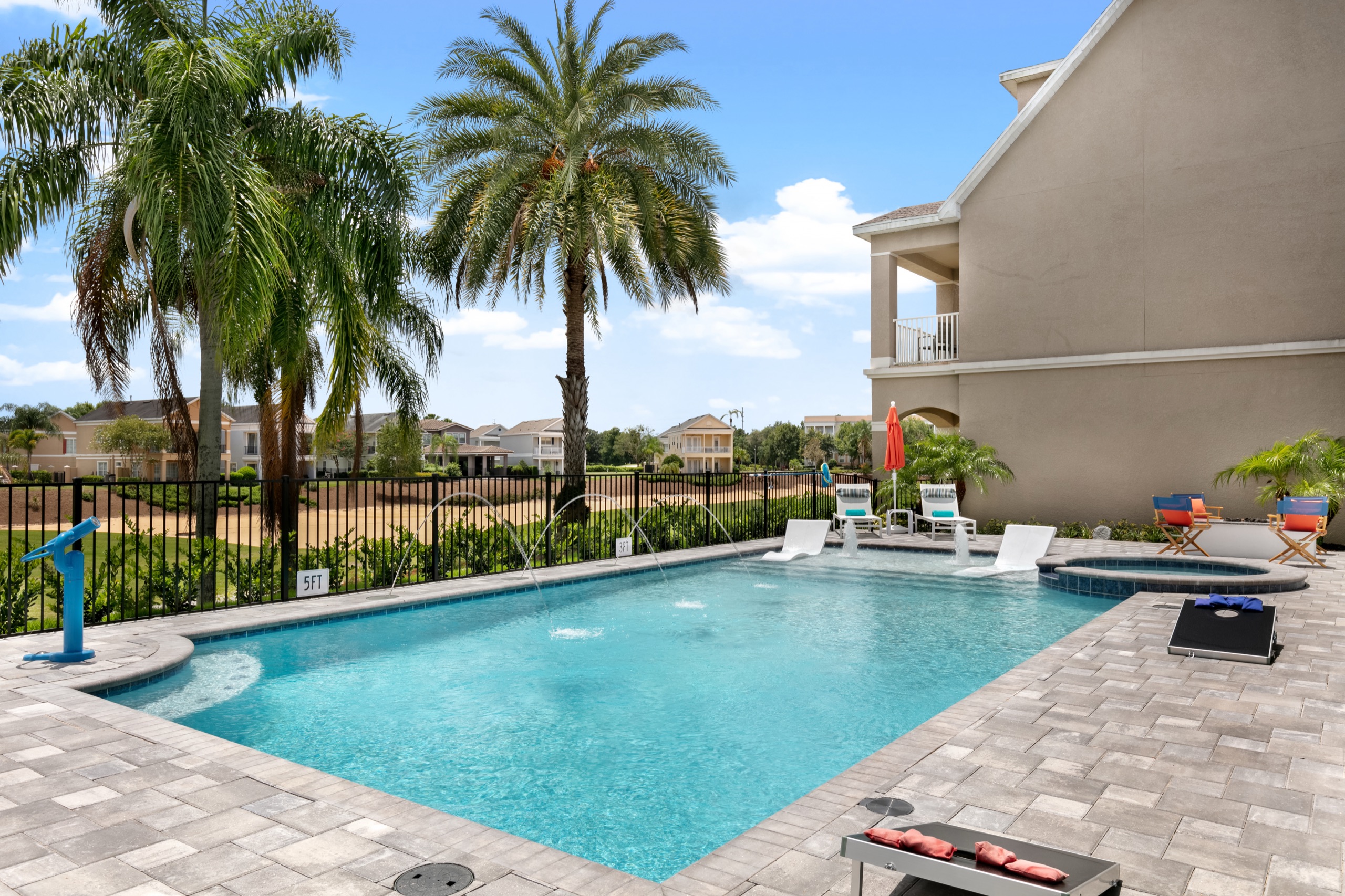 Golf-front pool with deck jets, an in-water spa, and paver deck with lounge chairs and cornhole under the palms