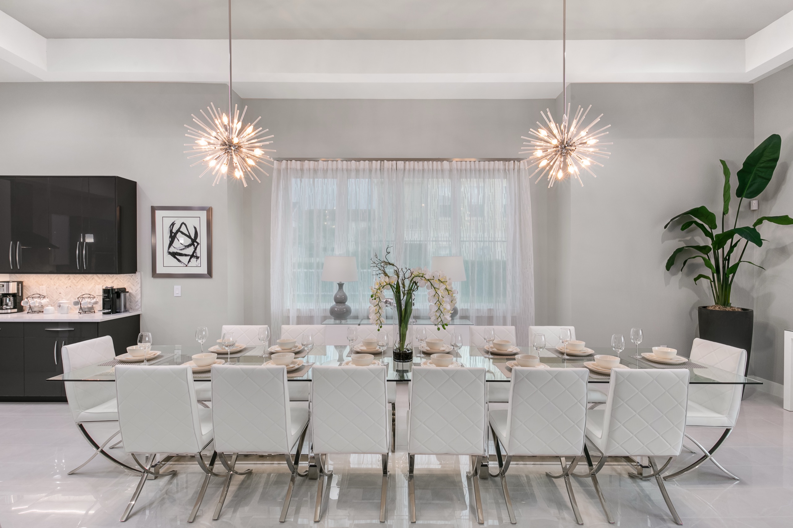 Formal dining room with a long glass table under twin sputnik chandeliers