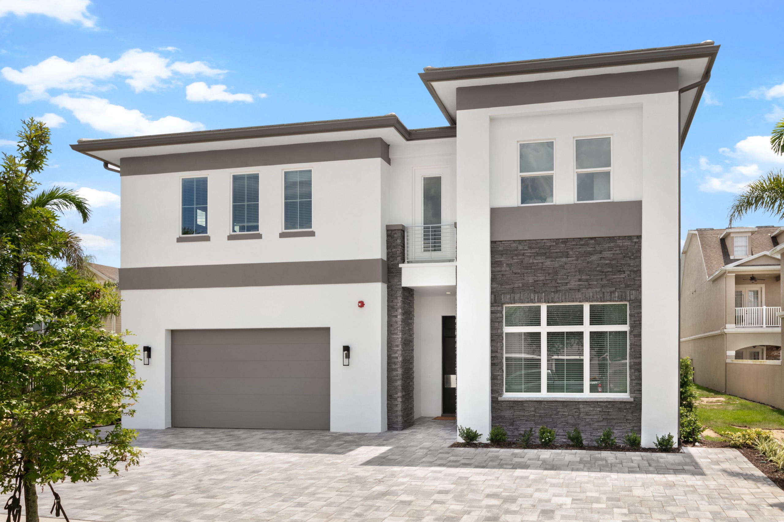 Contemporary white-and-gray front elevation with a two-car garage and paver drive