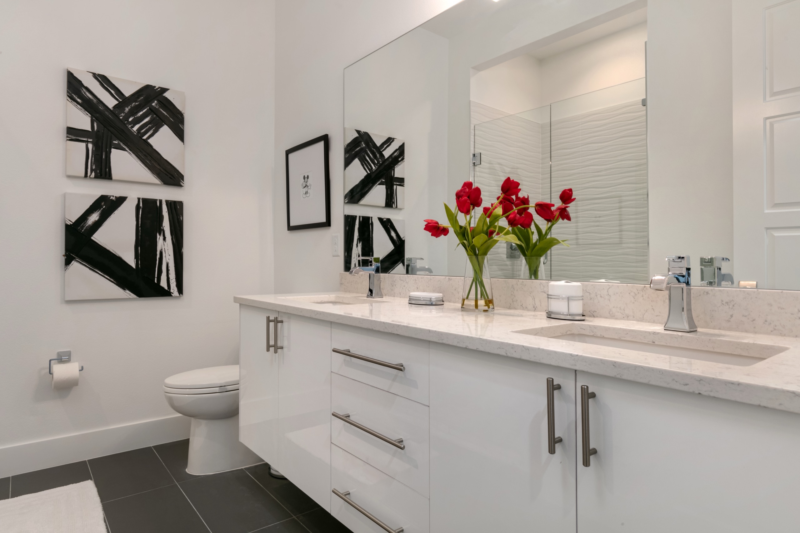 Mouse suite bath with a white double vanity, black-and-white abstract art, and fresh red tulips