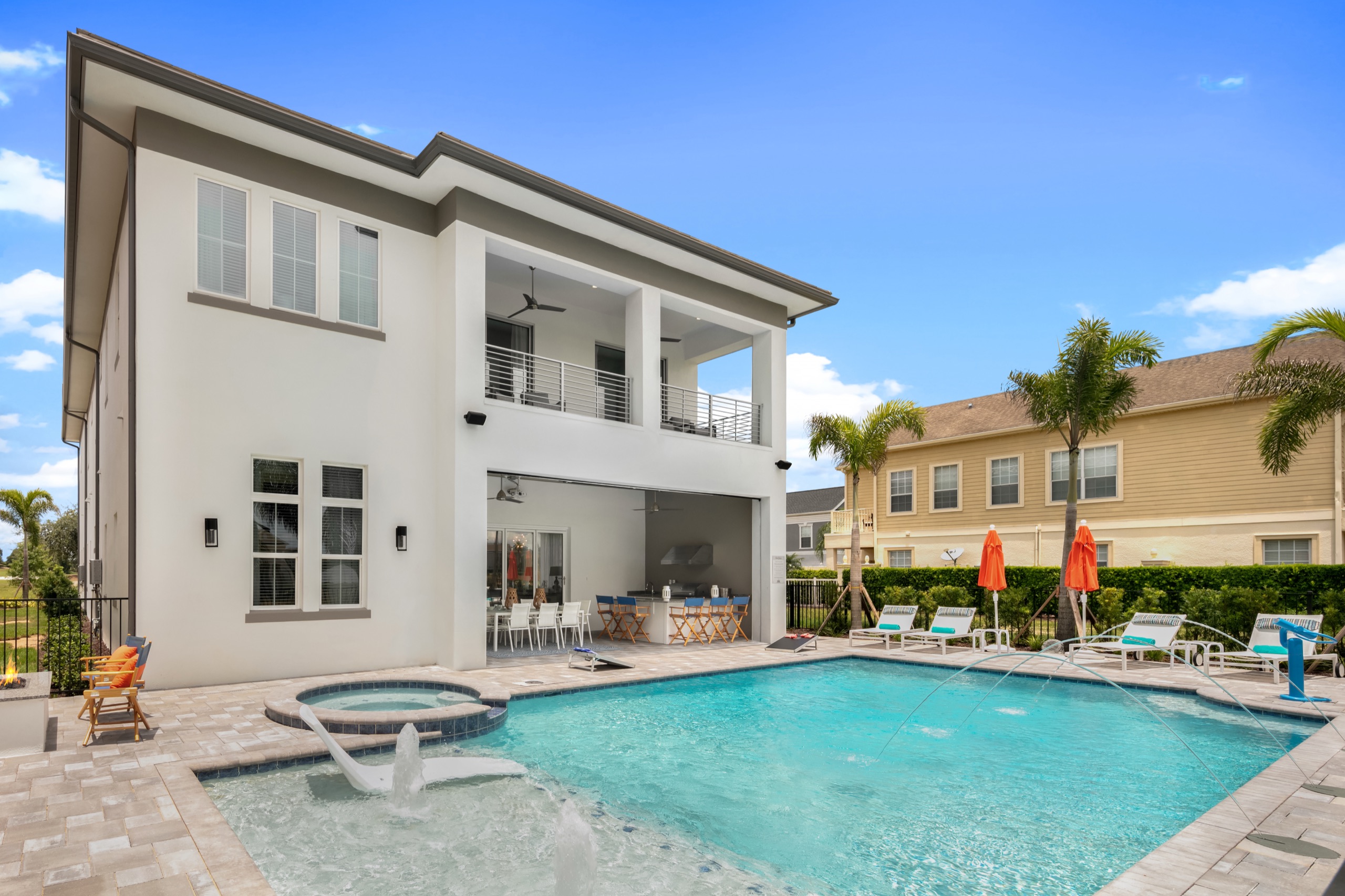 Rear elevation by day with the pool, spa, upper balcony, and the summer kitchen open to the deck