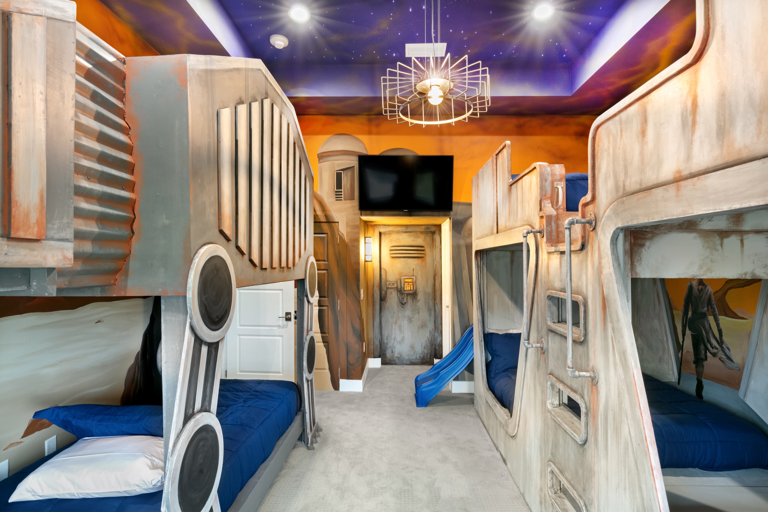 Spaceship bunk room with hand-sculpted bunks, a slide, and a painted desert-and-galaxy mural