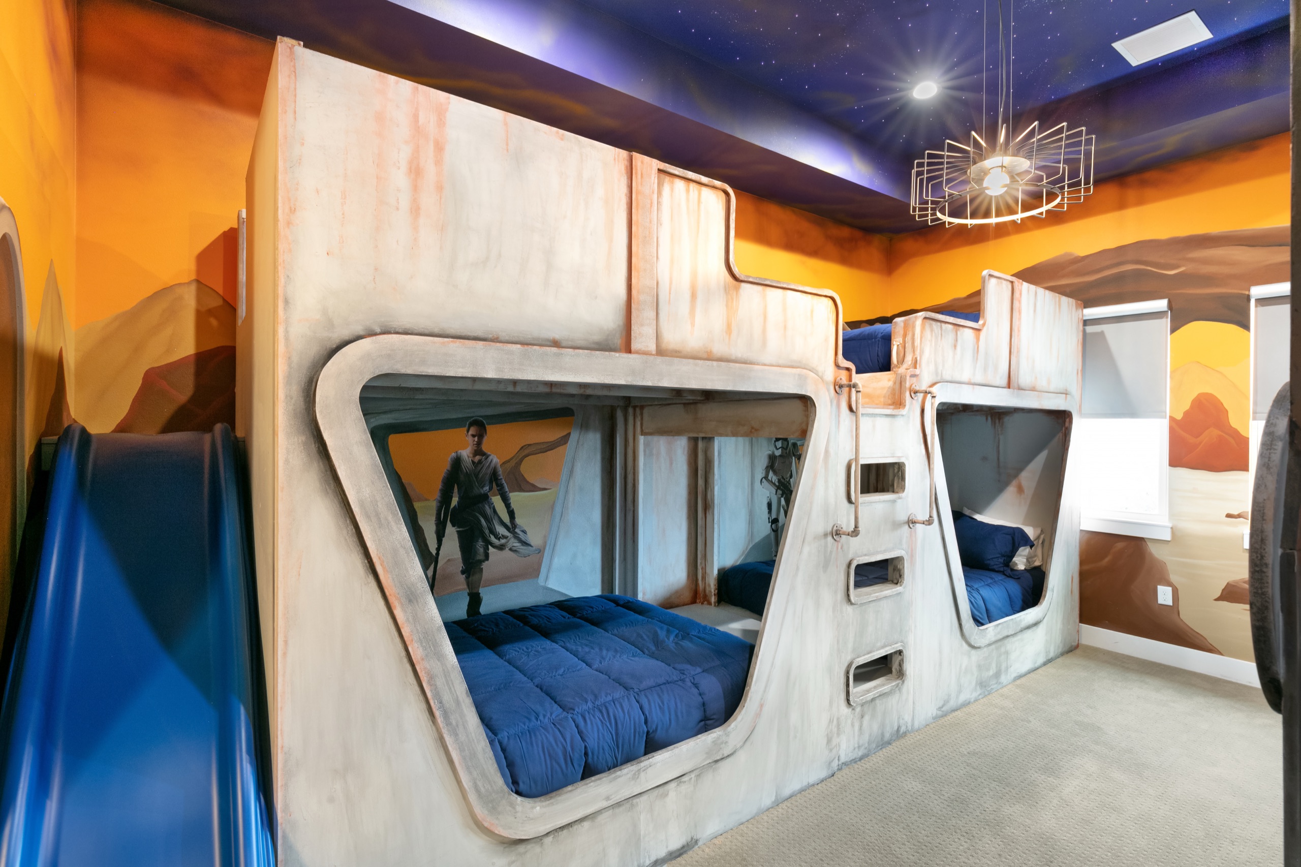 Cockpit-style bunk pods with a ladder, slide, and a desert-and-galaxy mural