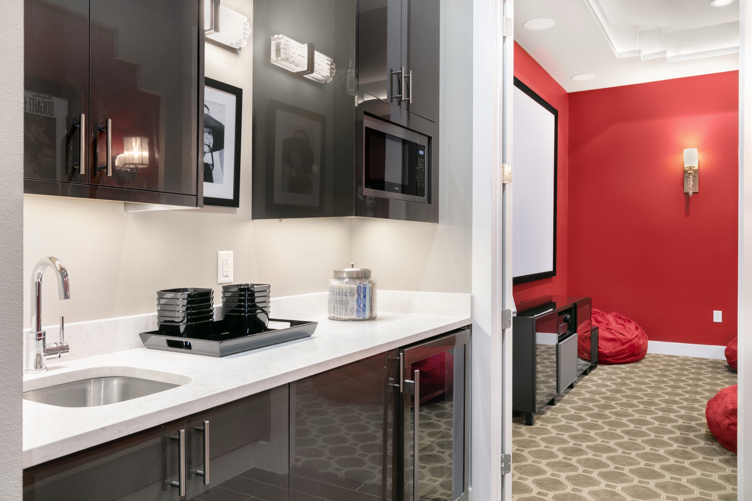 Wet bar with dark-gloss cabinetry just off the red-walled cinema