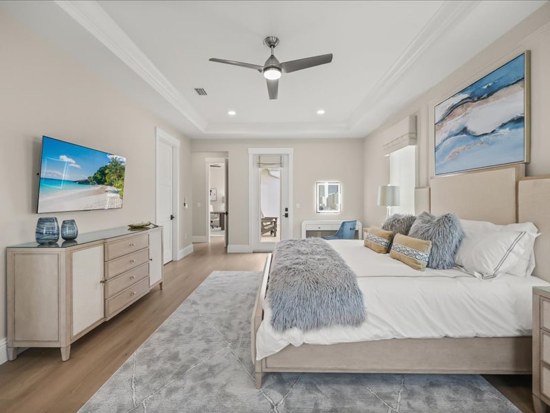 Primary suite with a tray ceiling, upholstered bed, and balcony doors