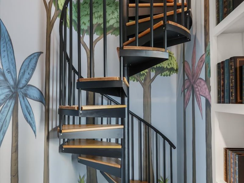 Sculptural spiral stair wrapped in a painted palm-tree mural, rising to the loft