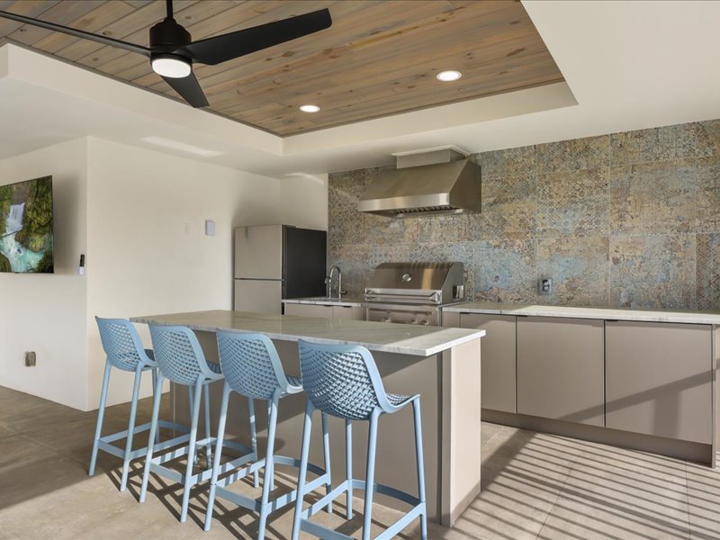 Summer kitchen with a grill and blue bar stools on the lanai